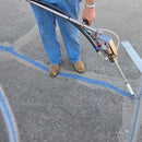 A worker in blue jeans and brown work boots operates the dispensing wand of an AST CMP 632 dispensing system, applying a sealant along a crack in a concrete surface.